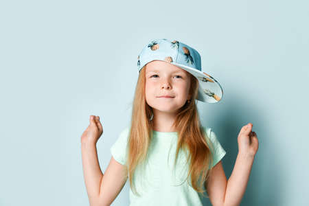 Cute blonde little girl in t-shirt, white pants and cap with pineapples print. She showing gyan...