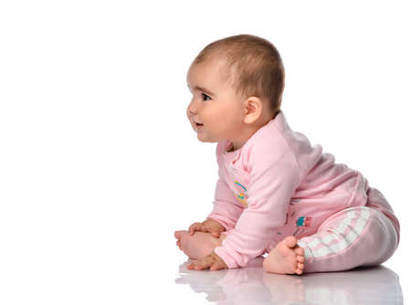 Child sits sideways looks away and smiles on a white background. Little beautiful cute barefoot girl dressed in pink clothes and looking at the free space for text.の写真素材