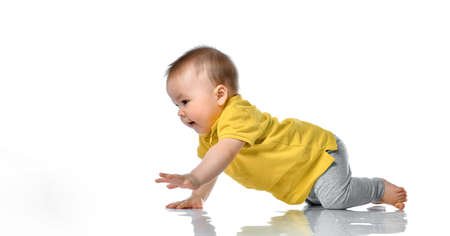 Cute positive little baby in a yellow polo and gray pants trying to crawl on the floor smiling and...