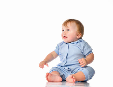 little blond boy with blue eyes sits barefoot in a pajama bodysuit and plays in the studio on a...