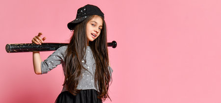girl in a dark dress, with a mesh skirt and sneakers, wearing a cap, holding a baseball bat on a pinkの写真素材