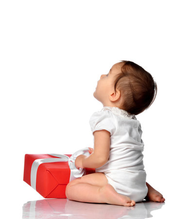 Surprised baby in jumpsuit sitting with gift box looking asideの写真素材