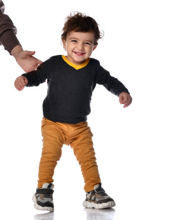 Happy little kid boy learning to walk standing on two legs against white background in studio.