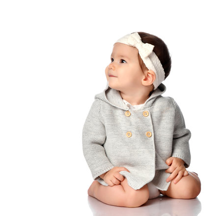 Happy smiling curious child in knitted clothes, headband isolated portrait. Excited infant child looking up over white studio background. Innocence, curiosity, childhood concept. Children's style, fashionの写真素材