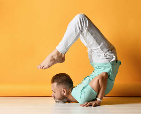Mature sporty man practicing yoga in Vrischikasana scorpion asana