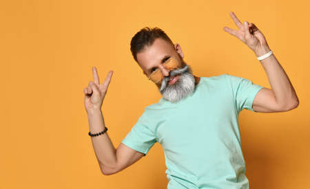 Portrait of a stylish man standing on an orange background and showing a peace sign.の写真素材