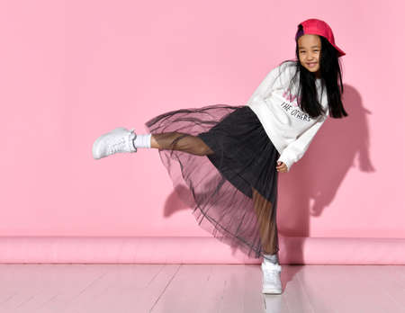 Side view of a little Korean girl model posing in the studio on a pink background raising her leg.の写真素材