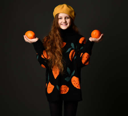 Portrait of a cheerful teenage girl with oranges standing on a black background.
