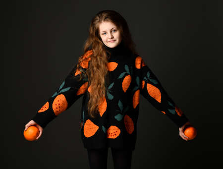 Portrait of a cheerful teenage girl with oranges standing on a black background.の写真素材