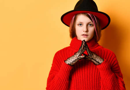 girl teenager in a fedora hat and a bright red sweater, she is on a yellow studio backgroundの写真素材