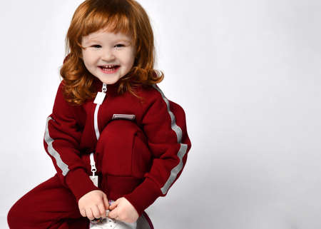 shy young redhead girl sitting on her knees and trying to button a sneaker, having fun and looking at the camera.の写真素材