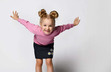 Smiling blonde girl with a stylish hairstyle in a pink blouse with a throat and a stylish skirt with daisy flowers and sneakers posing looking at the cameraの写真素材