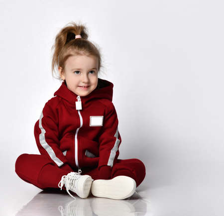 Little preschooler girl wearing warm tracksuit sitting over studio copy spaceの写真素材