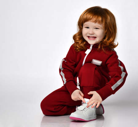 cute red-haired girl sits on one knee in a light studio. She is wearing a comfortable hoodie and sweatpants. Happy childhood and fashionable baby clothes.の写真素材