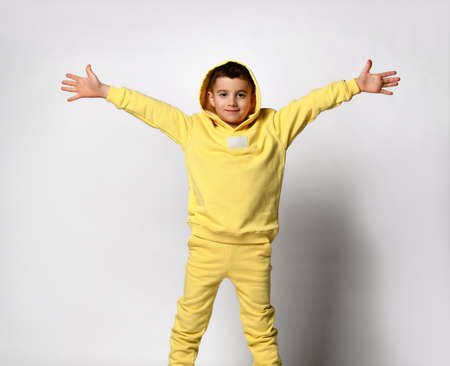 active teen boy, dressed in sportswear with a hood, having fun on a white background. The guy spread her arms like wings, free space for text. The concept of childhood and sportsの写真素材
