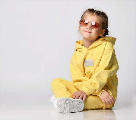 Portrait of a stylish little girl sitting and looking at the camera on a white background.の写真素材