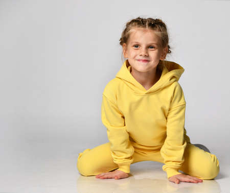Active little girl in a bright sports suit having fun sitting on a white background.の写真素材