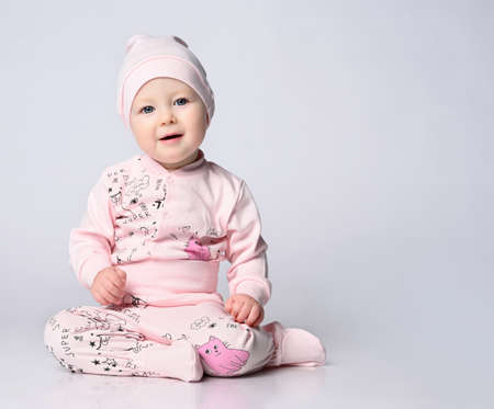 baby infant in a body with long sleeves and a shianishka, a matching hat, with a funny childish pattern on his clothes, sits on the floor in the studio.の写真素材