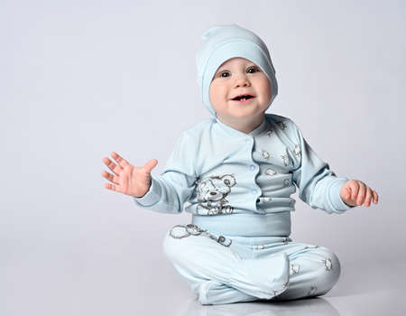 baby infant in a body with long sleeves and a shianishka, a matching hat, with a funny childish pattern on his clothes, sits on the floor in the studio.の写真素材