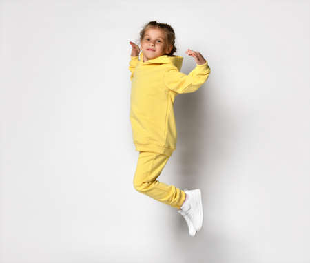 Playful cheerful girl in a stylish modern yellow sports hoodie and pants jumps high.の写真素材