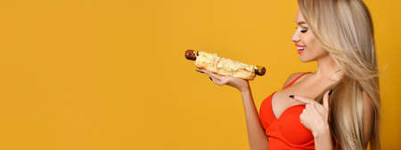 Glamorous sexy blonde looks seductively at a hot dog holding in her hand.の写真素材