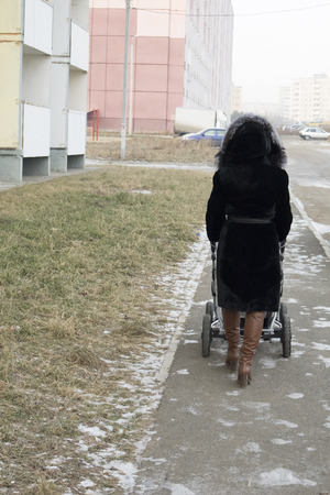 Mother walk with a baby buggy on city sidewalk. Season is near of November month.の写真素材