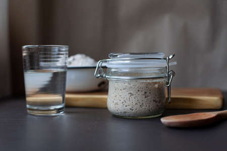 Active rye sourdough starter in a jar, a glass of water and a bowl with flour.の写真素材