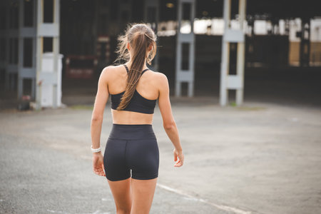 Young female athlete wearing black sportswear, engaging in various fitness poses outdoors against a modern industrial backdrop.の写真素材
