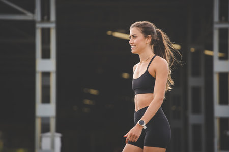 Young female athlete wearing black sportswear, engaging in various fitness poses outdoors against a modern industrial backdrop.の写真素材