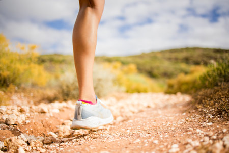 Female trail runner wearing black sportswear and a hydration vest, running through a scenic natural landscape on a rocky path.の写真素材