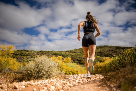 Female trail runner wearing black sportswear and a hydration vest, running through a scenic natural...