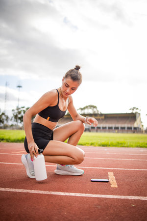 A focused female athlete captured during her training on the track, showcasing preparation, hydration, and determination in stadium setting. Highlights fitness, motivation, and athletic performance.の写真素材