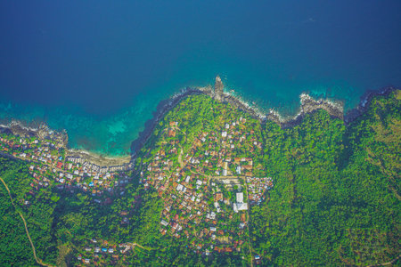 Aerial view of a coastal village surrounded by lush greenery and deep blue ocean.の写真素材