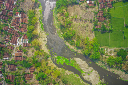 An aerial view showing a winding river surrounded by green vegetation and traditional homes.の写真素材