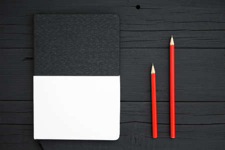 Blank notebook and pencil. Red pencil and blank black and white notebook on black wooden desk