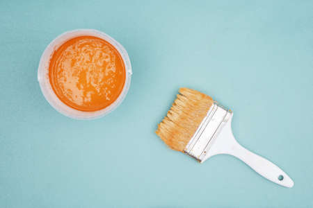 Paintbrush and bucket of ocher paint,top view.  Brush and paint on blue backgroundの写真素材