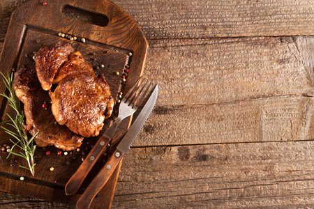 Grilled meat with spices on a wooden kitchen board. Roasted meat. Rib eye steak. Vintage style.の写真素材