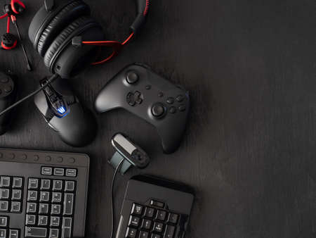 gamer work space concept, top view a gaming gear, mouse, keyboard, joystick, headset, mobile joystick, in ear headphone and mouse pad on black table background.