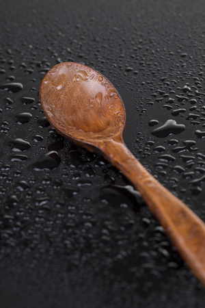 One wooden spoon with water drops on the blackの写真素材