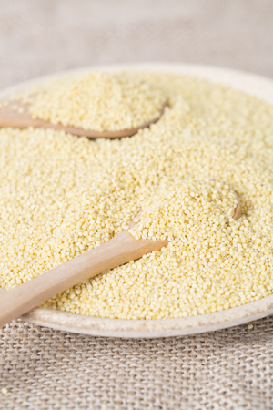 Yellow millet seeds in a wooden bowl on the tableの写真素材