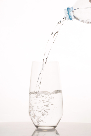 Pouring water from bottle into glass on white backgroundの写真素材