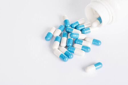 Blue pills in white pill bottle on white background.