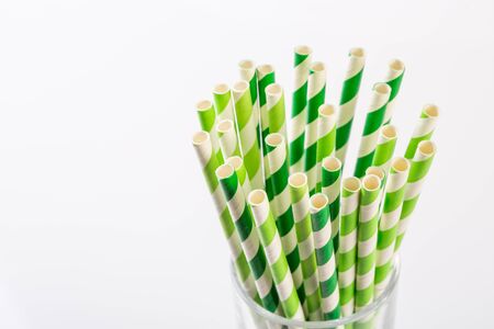 Green and white striped paper straws in a glass on white backgroundの写真素材