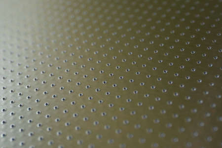 Industrial toned background in olive or bronze color. Perforated metal surface with many holes. Their ranks recede into the distance and form a perspective. Abstract aluminum backdrop or wallpaperの写真素材