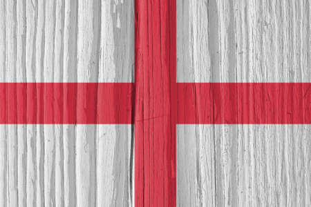 The flag of England on a dry wooden surface, cracked with age. It seems to flutter in the wind. Background, wallpaper or backdrop with national symbol. Saint George's Cross. hard sunlight with shadowsの写真素材