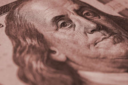 American paper money background. A $100 bill with focus on Benjamin Franklin eye. US banknote close-up. Dark brown tinted wallpaper about economy and the USA dollar. Macroの写真素材