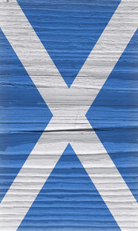 Flag of Scotland on a dry wooden surface. Vertical vintage backdrop. Rough board with cracks. The official Scottish symbol. Edge of the flag has faded like light vignettingの写真素材