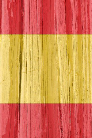 Flag of Spain on dry wooden surface, cracked with age. Vertical background, wallpaper or backdrop with Spanish national symbol. It seems to flutter in the wind. Hard sunlight with shadows on old woodの写真素材