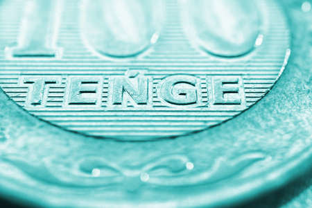 Translation: tenge. Fragment of Kazakh coin in 100 tenge. The name of the currency in Latin. Turquoise tinted background about economy of Kazakhstan. Light Kazakh money backdropの写真素材