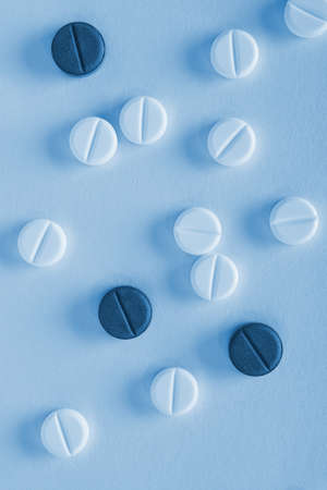 Blue tinted vertical background or backdrop on the theme of medicine, health care, drugs, pharmacology. Light and dark pills lie on a sheet of paper. close-up. Top view from above. Macroの写真素材
